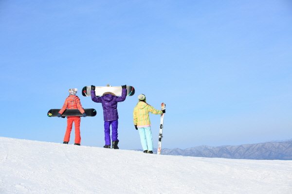 Three people standing on a snowy field holding a board.